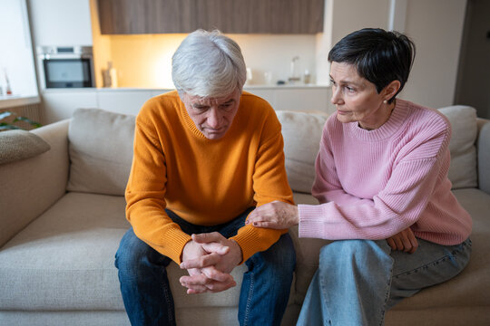 Depressed husband sits on couch, overwhelmed by work problems struggles. Supportive mature wife gently holds his hand, comforting consoling through financial and life challenges, frustrated spouse