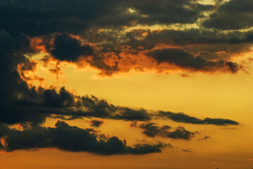 At sunset, dramatic clouds streak across the golden sky, creating a vivid contrast between shadows and highlights. Warm shades of orange and yellow mingle with darker cloud formations.