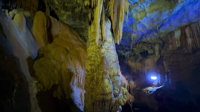 The bright and colorful Abrskil cave. A gallery-type cave in the mountains of Abkhazia with many stalactites and stalagmites, colorful lighting. Otapskaya (Otap cave). 4K