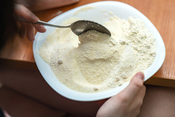 A metal spoon mixes sugar and semolina flour in a white ceramic bowl, capturing the preparation of...