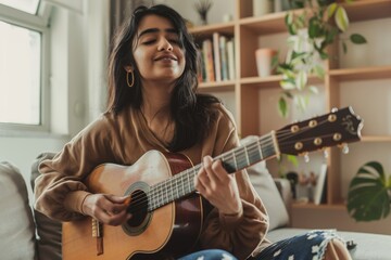 Portrait of a blissful indian woman in her 20s playing the guitar isolated on crisp minimalistic living room