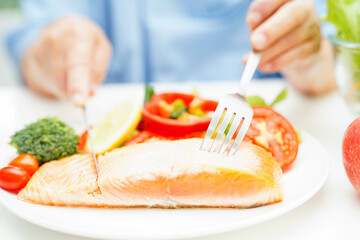 Asian elderly woman patient eating salmon stake and vegetable salad for healthy food in hospital.