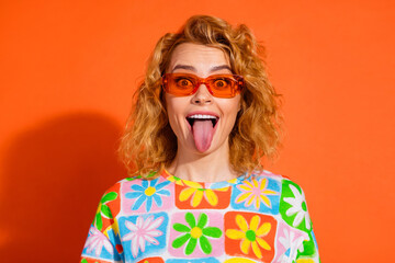 Obraz premium Vivid Portrait of a Cheerful Young Woman Showing Her Tongue Against an Orange Background