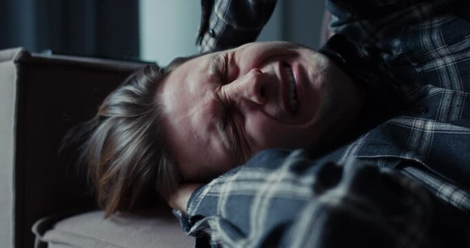 A man cries and lies on the sofa covering himself with his hands at home