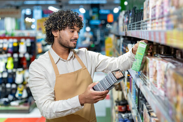 A friendly worker, wearing an apron, is reviewing products on the shelf at the store. He carefully...