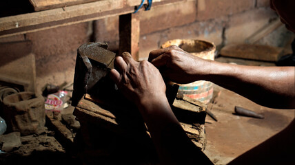 Dirty hands of worker making clay statue in Balinese style in dark workshop