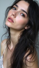 Obraz premium This stunning close-up captures a young woman with long, tousled dark hair and a soft, natural makeup look. Her expressive gaze and delicate features evoke a sense of beauty and serenity, inviting
