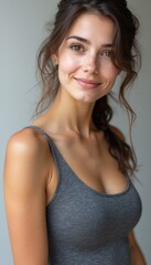 Fototapeta premium A beautiful young woman with long, flowing hair and a gentle smile radiates confidence and warmth against a soft, neutral background. Her casual gray tank top complements her natural beauty, creating