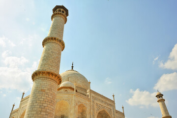 Fototapeta premium Low-angle view of the majestic Taj Mahal in Agra, India, showcasing its stunning minaret and dome of the mosque, mausoleum, and tomb with Mughal Islamic architectural style under a clear blue sky.