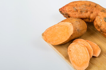 Raw sweet potato on a cutting board, whole and sliced. Horizontal, free space for copying.