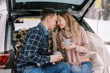 Man and woman touch foreheads while sitting with coffee mugs in car trunk in winter park © VolodymyrNadtochii