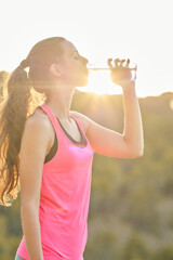 Young woman drinking water at sunset while enjoying outdoor fitness and hydration