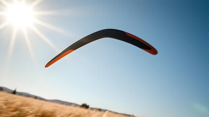 Flying boomerang in mid-air above a sunny field with clear blue sky and sunlight in background.  