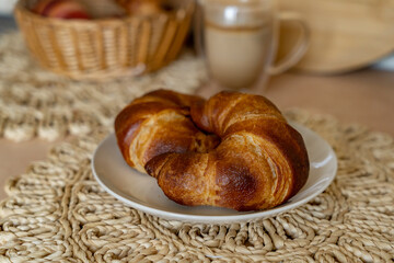 Freshly baked croissants on a plate and a glass of latte on the background. Homemade breakfast with croissants and coffee.