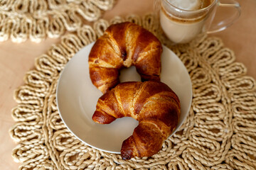 Croissants on a plate on a blurred background with a cup of cappuccino. Homemade baking for breakfast.
