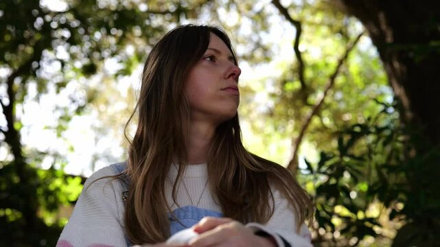 Young European woman with long hair in denim dungarees siting on the steps in the shade of Japanese garden and looking around. Japanese style hut in a blurred background. Peaceful green environment.