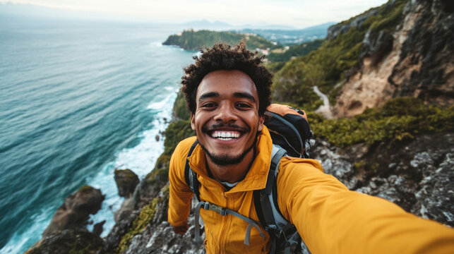 A man in a bright yellow jacket smiles broadly while standing on a rocky cliff by the ocean. The sun shines, illuminating the stunning coastal landscape around him.