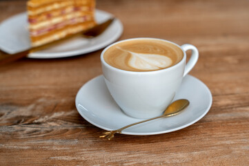 Cup of coffee, cappuccino with a piece of cake on a wooden table in a cafe. 