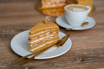 Piece of honey cake on blurred background of cappuccino cup on wooden table. Cafe concept.