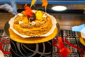a mona de pascua, a cake eaten in Spain on Easter Monday, topped with a chocolate chick, on a rustic wooden surface full of decorated eggs and feathers of different colors