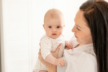 A mother gently kisses and hugs a newborn baby holding him in her arms in a bright bedroom, motherhood or a happy young family with a small child. High quality 4k footage