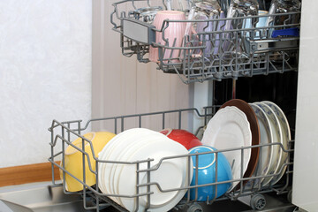 Open dishwasher showing colorful plates, bowls and cups ready for washing