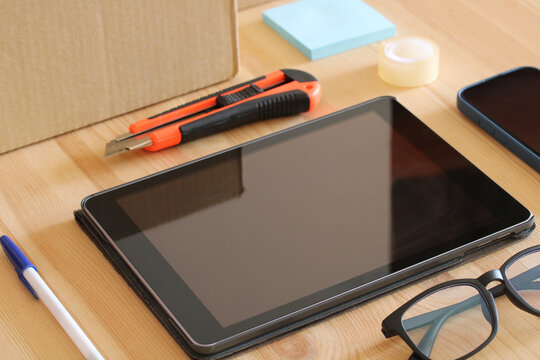 Tablet, smartphone, box cutter and eyeglasses lying on wooden desk - Powered by Adobe