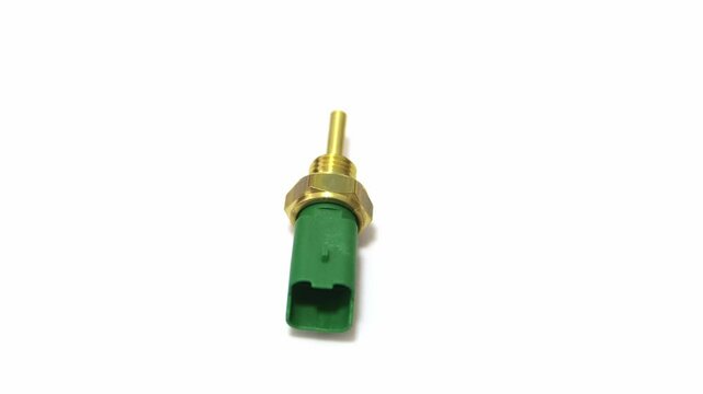 Car temperature sensor, a precision automotive component. Made of brass and green plastic, with an electrical connector and thread for engine installation. Isolated on a white background.