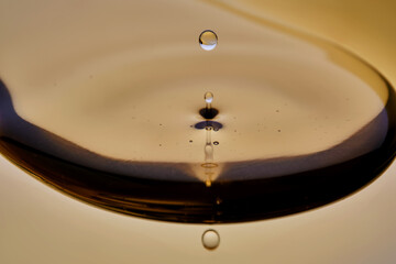 Texture of cosmetic oil with falling drop on golden background.