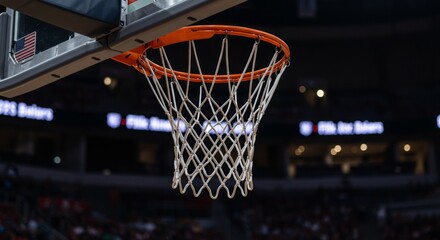 Basketball hoop with white net in professional sports arena during game. Close-up view of orange rim against dark background with American flag. Sports equipment in indoor stadium.