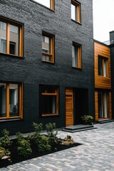 Modern architectural design features contrasting materials and textures in a residential building courtyard with greenery and cobblestone pathways, creating a stylish urban atmosphere