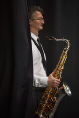 Fototapeta premium Vertical side view of contemporary jazz male player of middle age wearing formal white shirt and black tie steps onto stage from behind curtain