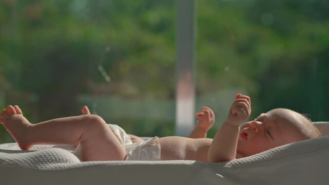 A newborn baby rests in a baby cocoon near an open sunlit window, absorbing natural sunlight for a healthy dose of vitamin D.