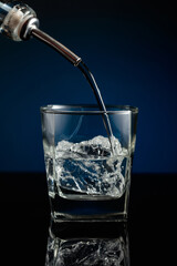 Crystal clear vodka being poured over ice in a glass.