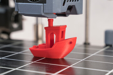 Red 3D printed boat is created on a printing bed with precise layer formation in a modern workshop