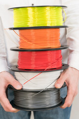 Caucasian man holds a stack of plastic filament spools for 3D printing.
