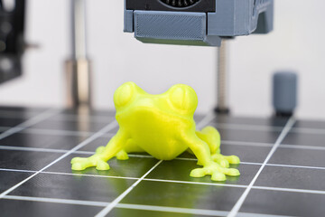 3D printed yellow frog is created on a printing bed with precise layer formation in a modern workshop