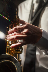 Obraz premium Vertical close up shot of professional male saxophonist playing intricate jazz melody pushing keys of instrument with nimble fingers creating enchanting music under bright spotlight, lens flare effect