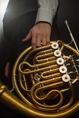 Fototapeta premium Vertical close up on hand of male musician holding shiny French horn with exquisite engraving on valves while preparing before brass instrument performance on stage