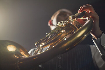 Low angle shot of male musician pushing valve levers of golden French horn while performing deep...