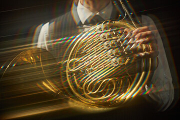 Midsection of unrecognizable person playing golden double French horn shining in bright beams of...