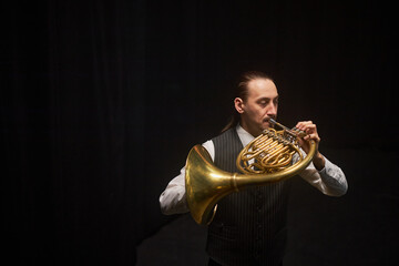 Medium full shot of focused male French horn player performing jazz music on wind instrument...