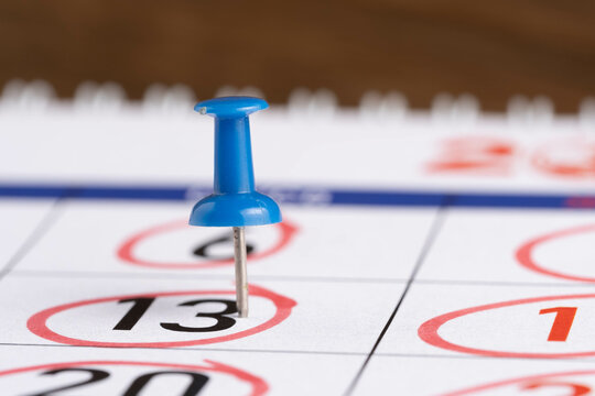 Calendar with blue push pin on wooden background, closeup.
