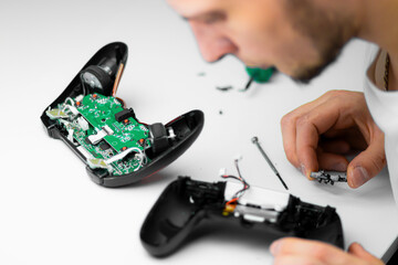 A man in a white shirt repairs a black gaming controller with a small screwdriver. The close-up shot captures his hands and the device against a clean white background.   © Anastasiia