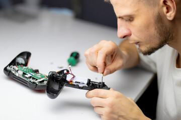 A man in a white shirt repairs a black gaming controller with a small screwdriver. The close-up shot captures his hands and the device against a clean white background.   © Anastasiia