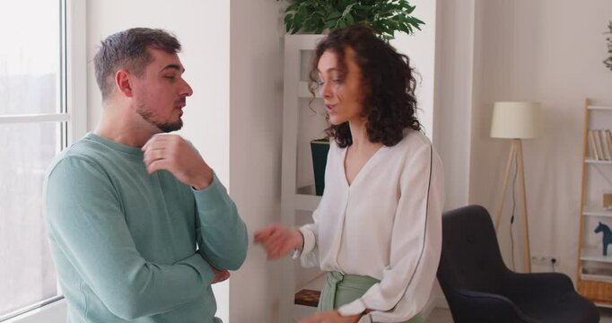 Unhappy annoyed family couple standing by window, facing relationship problems and arguing with each other. Frustrated husband and wife with marriage problems quarreling and shouting during conflict.