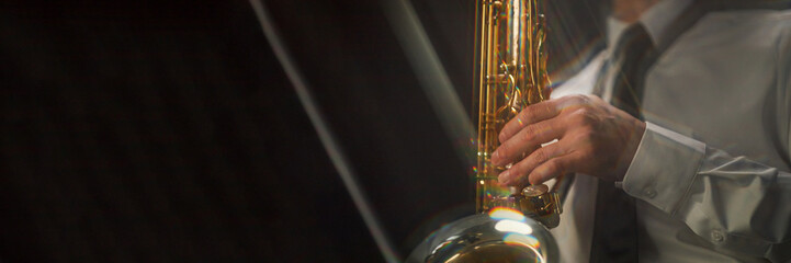 Website header shot of shiny saxophone in hands of male musician playing enchanting jazz music...