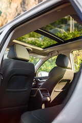 View through SUV doorway with open sunroof, showing black leather seats and headrests. Scenic...