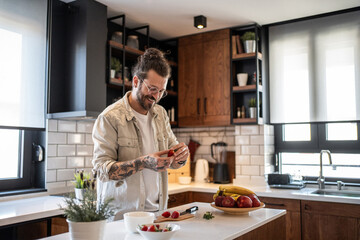 Smiling man preparing strawberries for a healthy meal in modern kitchen