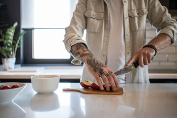 Tattooed chef skillfully slicing fresh apples in modern kitchen